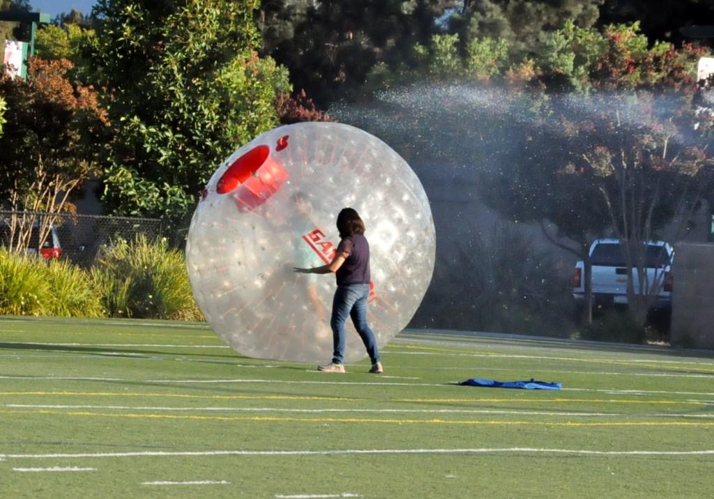 A student pushes her friend in a hamster ball as they roll through the sprinklers on the field during the First Friday back to school social event. First Friday took the place of the back-to-school social this year.
