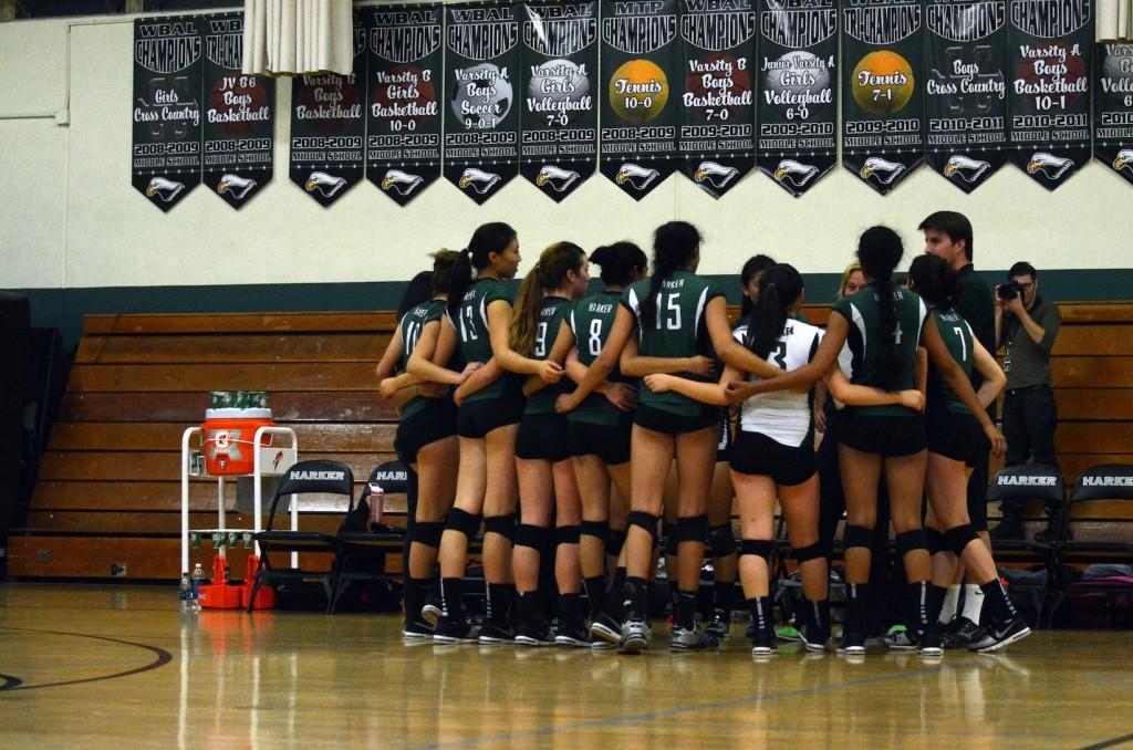 The varsity volleyball girls come together in a huddle before their senior night game, holding each other to show their team support. 