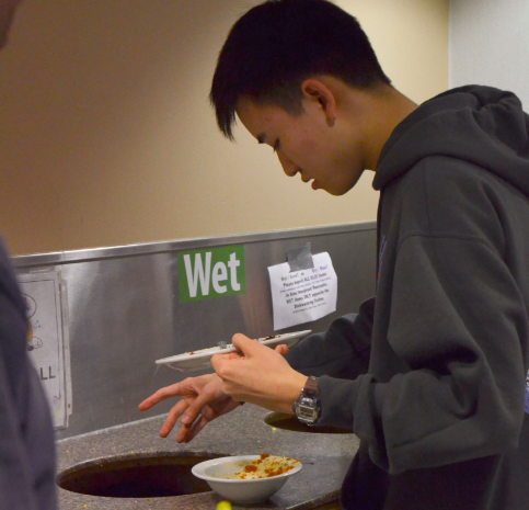 Eric Yu (11) throws away his compostable trash in Manzanitas wet waste bussing station. Physics teacher Christopher Spenner (pictured) and other faculty members supervised the disposal process.