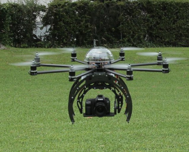 A+drone+carrying+a+camera+hovers+over+grass.+Besides+military+operations%2C+drones+have+also+been+for+topography+and+crop+surveying.