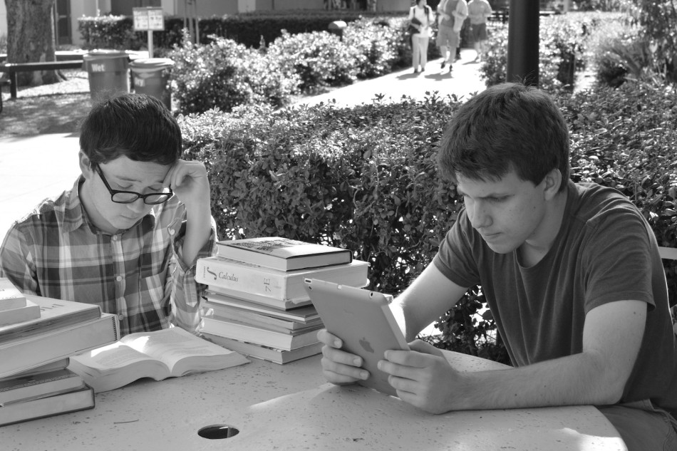 Damon Aitken (12) studies for a test using physical textbooks, while Nicky Semenza (12) opts to use an iPad instead. Digital textbooks have become more prevalent among Upper School students since the administration allowed e-readers to be used in classrooms one year ago.