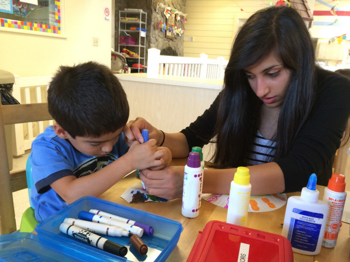 Avni Barman (12) helps out a child with his art project. The projects are done with supplies like glue, washable markers, and paper.
