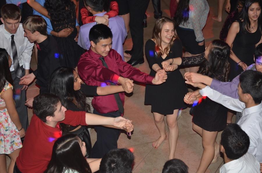 A group of students hold hands while dancing to the music in a circle with vibrant lights shining on them. The Winter Ball took place in Nichols Hall on Saturday, Jan. 17.