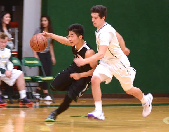 Justin Yen (12) dribbles the ball down the court, protecting it from a Pinewood player. The boys lost 52-64 on Friday.