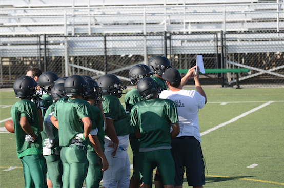 Players listen to the head coach as he provides a defensive game plan for them to practice.