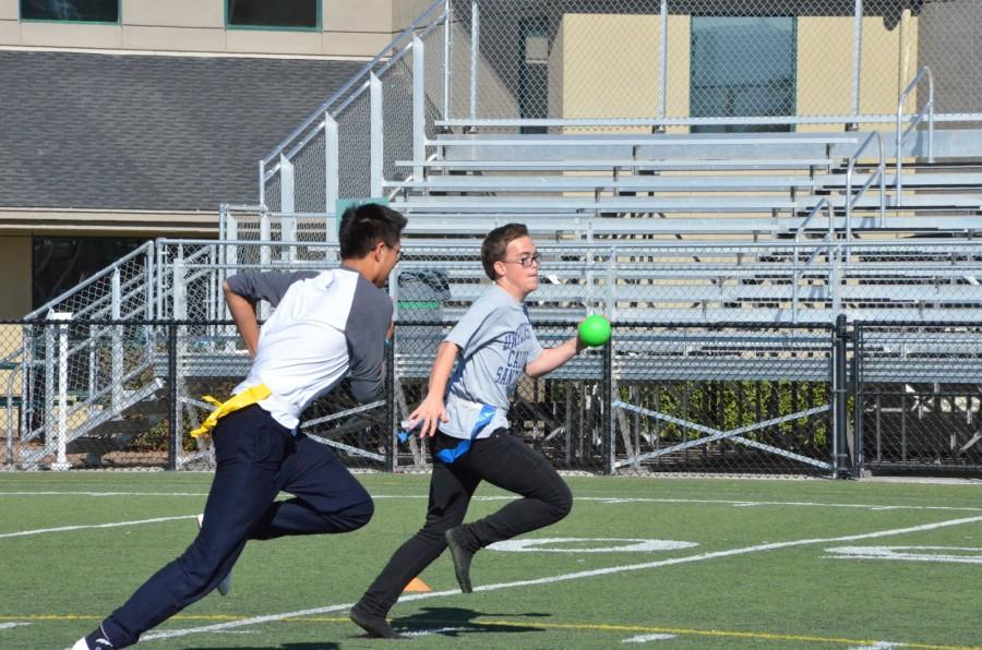 Senior Ryan Fernandez dashes to his side of the field with a ball in his hand while Brandon Mo (10) chases after him to take off one of his flags. Each class competed against each other during long lunch in a game of capture the flag.