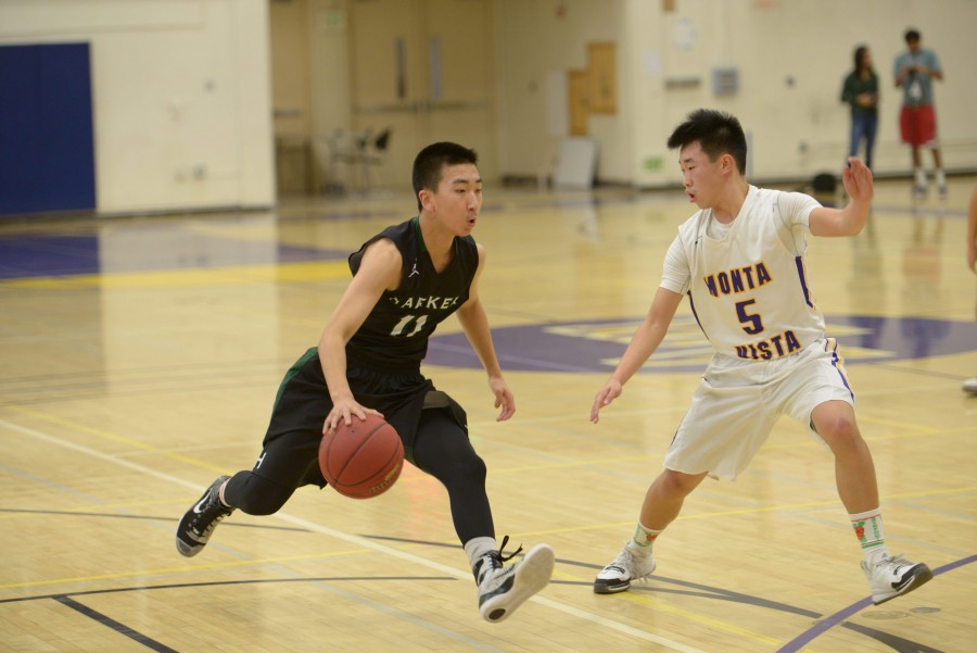 Roy Yuan (9) dribbles the basketball as he runs towards the basket and a guard from Monta Vista runs with him, trying to hold back Roys shot. The Eagles scored more assists but fewer rebounds and steals, and they lost 50-56 to their opponents.