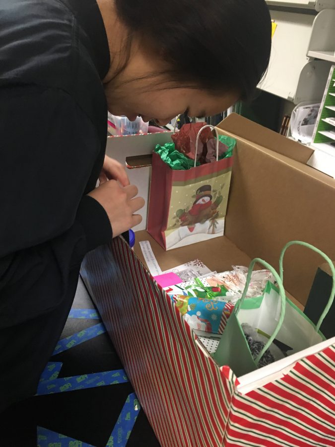 Ashley Jiang (11) peers into a box holding gifts from the journalism programs annual secret Santa gift exchange. As winter break approaches, upper school students and faculty organize exchanges like secret Santa and white elephant to celebrate the holidays.