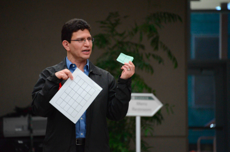 SNHS advisor Abel Olivas holds up a bingo card and bingo clues while explaining the rules of the game. Event attendees also participated in another activity where they attempted to identify the genres of a series of Spanish songs.