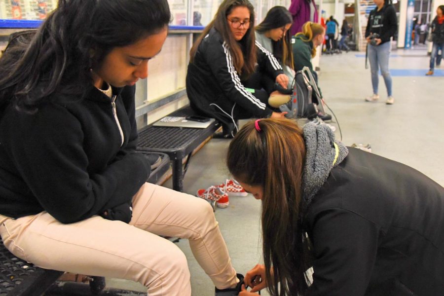 Cas Ruedy (10) helps Divija Bhimaraju (12) lace up her skates at the benches by the rink. Todays ice skating trip was open to all students.