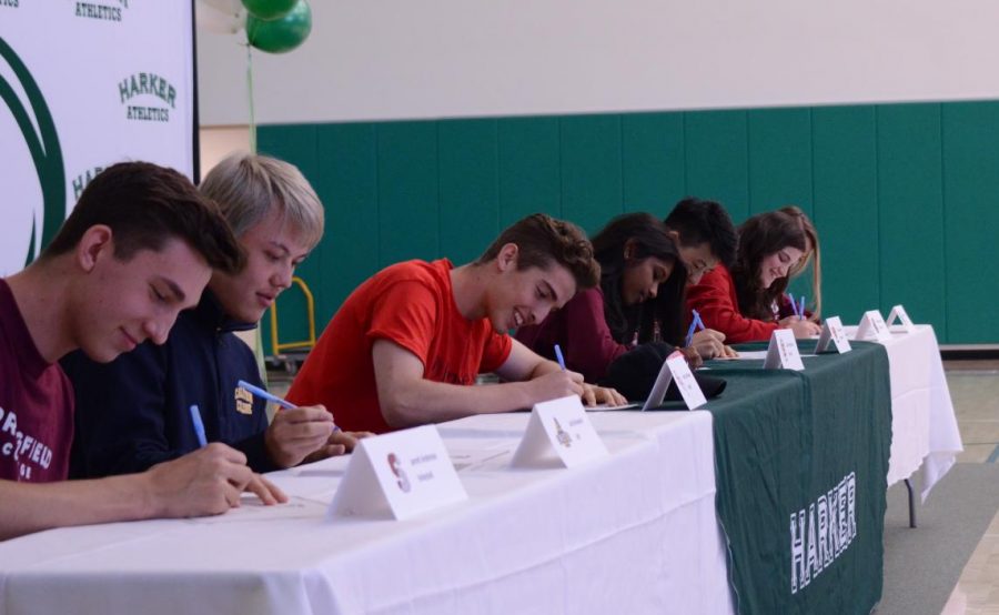 The seniors, sitting at a long table with name tags featuring their name, sport and college, sign their letters of commitment to play in college. Signing day was held in the athletics center during long lunch at 12:45 on Thursday, April 18. 