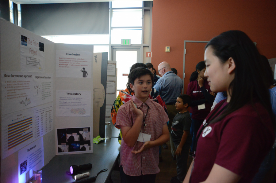 Middle schooler Ben Lee explains his project to Alice Feng (9). He explored the properties of prisms.