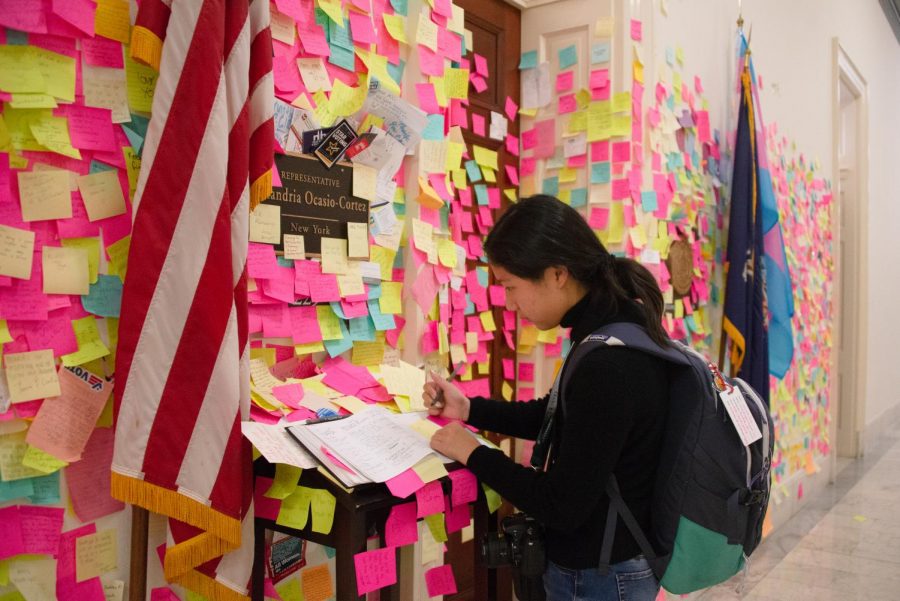 Nicole Tian (10) writes a message on a Post-It note to add to the mural of Post-Its around Rep. Alexandria Ocasio-Cortezs (D-NY) Cannon office door. 