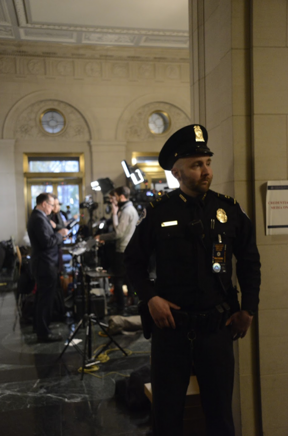 A security guard keeps watch while news anchors and reporters wait for updates behind him. More security measures were implemented in the building due to the impeachment hearings.