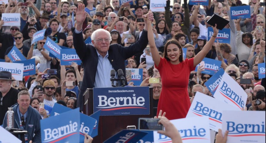 At the start of his speech, presidential candidate Sen. Bernie Sanders joins hands with Rep. Alexandria Ocasio-Cortez as the crowd shows their support. This rally was the conclusion of Sanders campaign across Southern California over the past week.
