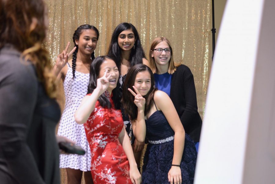 A group of freshmen pose in front of the photo booth, smiling and laughing as they playfully take pictures of themselves at the dance.
