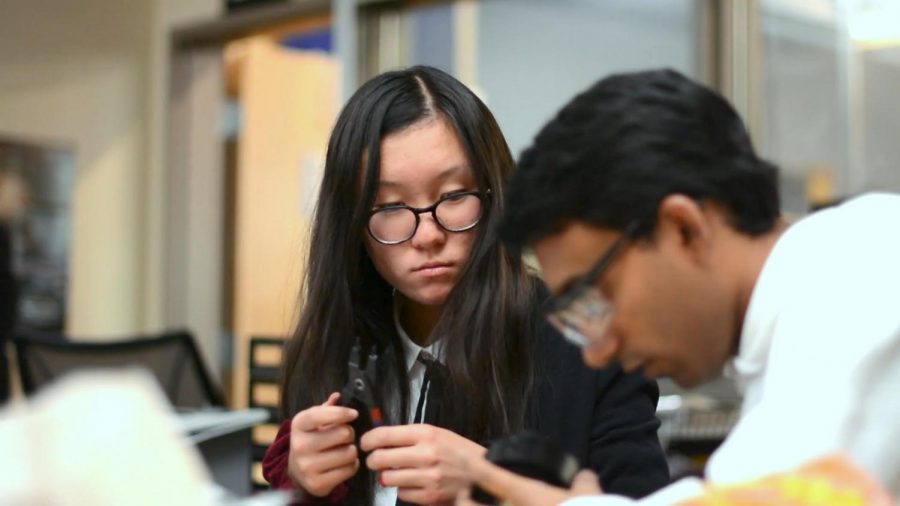 Alina Yuan (10) watches Anand Rajamani, one of the Harker Robotics mentors. There are five mentors in the robotics program that teach members.