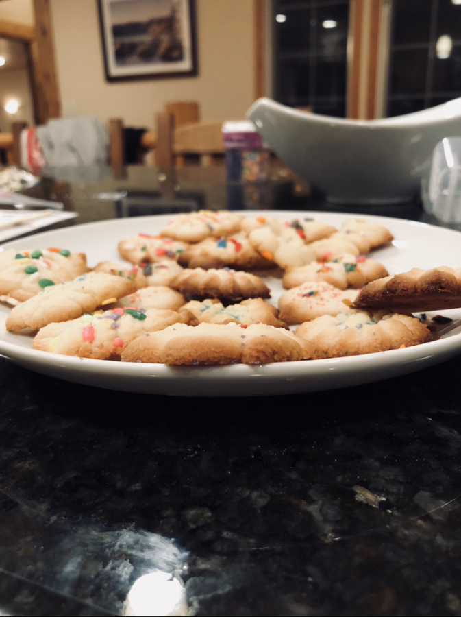A plate of Christmas sugar cookies sits decorated with colorful sprinkles sits on a marble table. I baked these treats when I was in Heavenly, spending the winter holiday season with my friends and family.