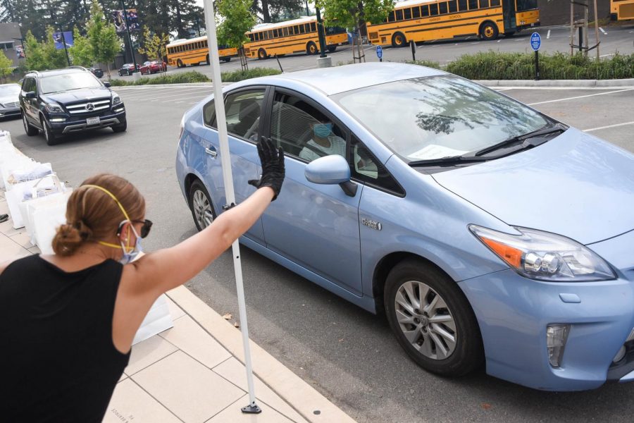 Upper school librarian Meredith Cranston waves to a student driving by. Students drove by the front loading zone on Saturday to receive supplies for the upcoming school year.
