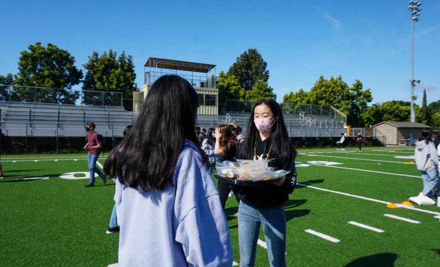 Freshmen class council officer Ella Lan (9) offers individually packaged donuts to a student on April 22 during the morning class spirit activity.