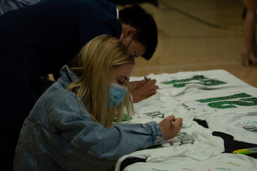 Emma-Leigh Stoll (12) and Ethan Choi (12) sign their names on a T-shirt at the Lifer Event, an activity hosted by upper school alumni directror Kristina Alaniz to honor the 53 lifers in the senior class.