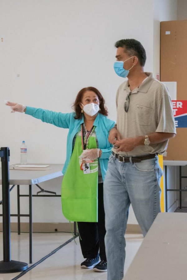 A volunteer guides a voter to the ballot boxes yesterday at the St. Francis of Assisi Parish polling center in San Jose. All active registered voters were mailed a vote-by-mail ballot before the election, but also had the ability to vote in person.