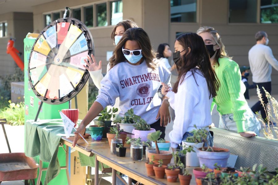 Medini Halepete (10) adjusts the Green Team booth, which featured a spin-the-wheel with environmental questions and potted succulents in front of Nichols Hall. Fourteen different upper school clubs hosted booths in or in front of Nichols and in the quad, with posters and interactive games or activities, many designed for lower or middle school students.