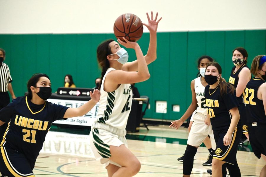 Lexi Nishimura (11) holds the ball up just before attempting a floater shot while an offensive player tries to guard behind her.
