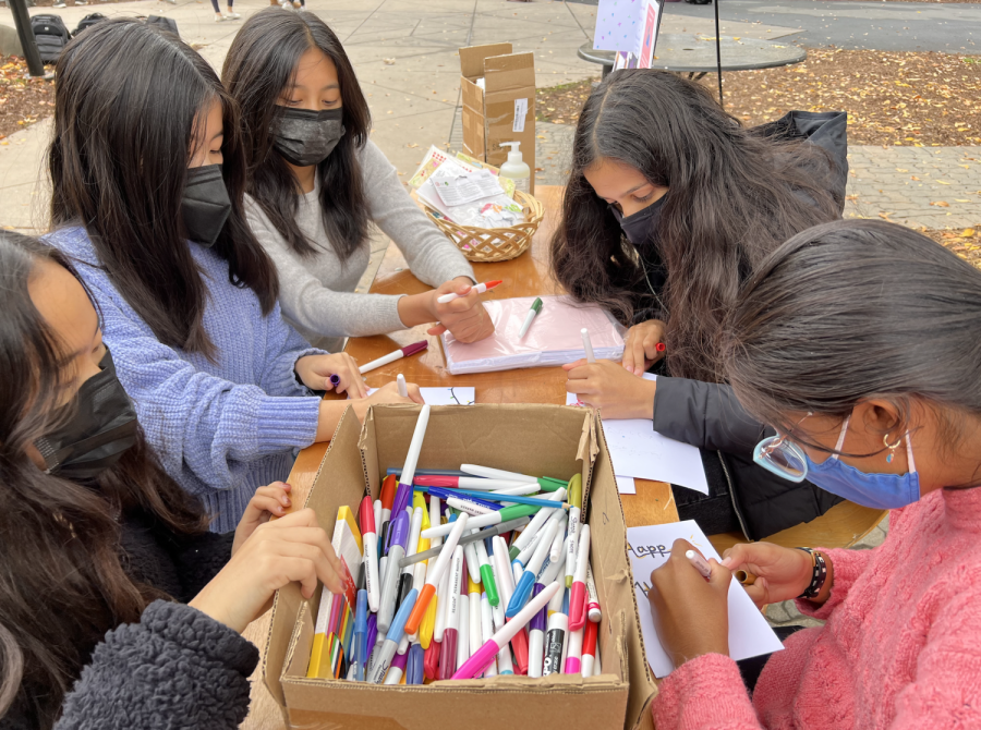 Sophomores Selina Xu, Meishin Yen and Claire Miao work on cards at a table outside of Manzanita with chapter president Ishani Sood (10) and vice president of outreach Trisha Iyer (10) during the upper school Women for Women Internationals holiday card writing event on Dec. 7.