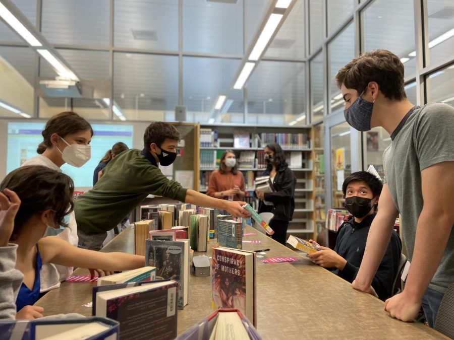 Rupert Chen (11) reaches to hand a book to Nicholas Wei (11) as their fellow Book Party attendees share their thoughts on the books featured at the gathering.