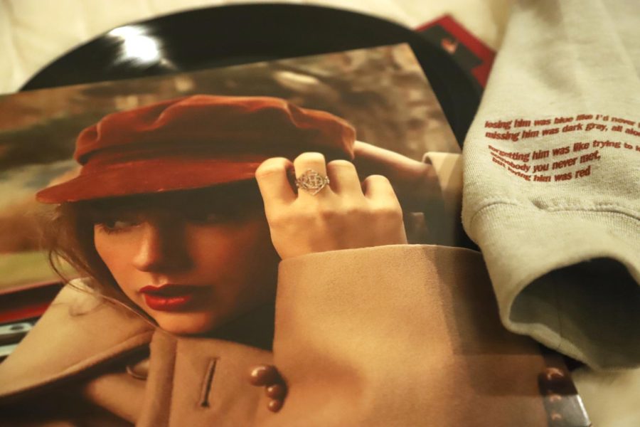 A sweatshirt sleeve of Taylor Swifts Red (Taylors Version) merchandise rests on a vinyl disc and jacket of the album. Swift re-recorded Red, and released it as Red (Taylors Version) on Nov. 12, containing a total of 30 tracks.