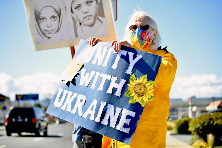 A protestor in a yellow coat holds up a Unity with Ukraine sign in solidarity with Ukrainian citizens and immigrants who still have family in the country. 