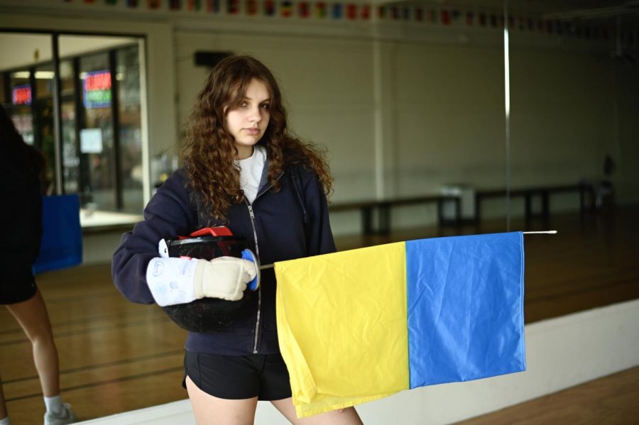 Kristina Petrova, a 17-year-old fencer from Ukraine, stands with the Ukrainian flag and her fencing gear at Maximum Fencing Center in Mountain View, California. Kristina crossed the Ukrainian border into Slovakia on Feb. 25.