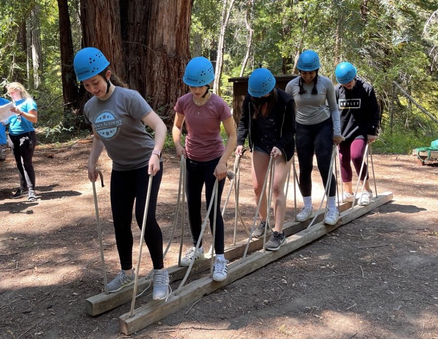 Sophomores work together to walk with long wooden planks beneath their feet during their class trip on Aug. 18. After traveling to the ropes course, students split into groups based on their advisories to engage in various team bonding activities.