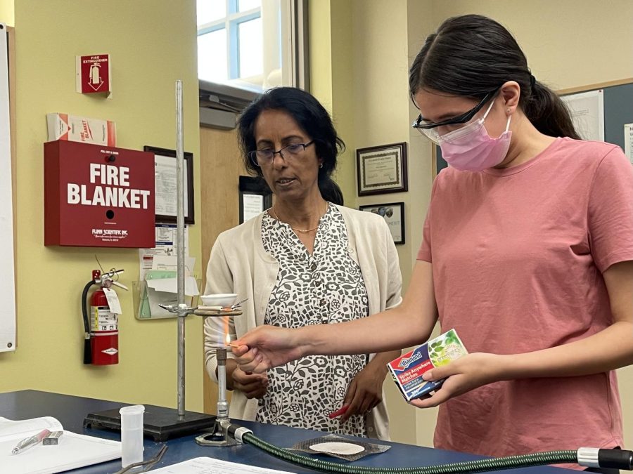 Upper school chemistry teacher Dr. Mala Raghavan helps Jacqueline Soraire (11) light the Bunsen burner during the lab on Wednesday. Advanced Placement (AP) Chemistry class for juniors and seniors conducted their first experiment of the year on Wednesday.