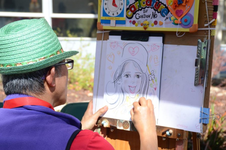 Caricature artist Gordon Ng draws a representation of the subject sitting behind the easel. At Harker Day, several caricature artists had booths in the Eaglet Zone, which was located at the Quad.