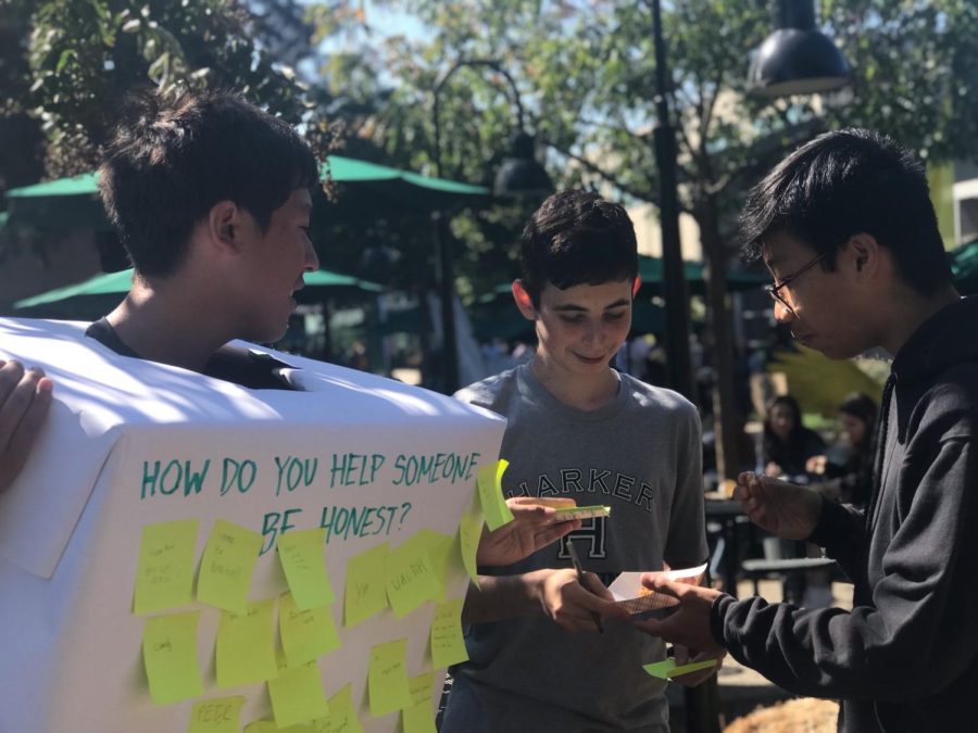 Harriss Miller (10) and Nelson Gou (10) write on Marcus Blennemans (10) box. Students answered prompts about honesty on post-its and pasted them on the boxes to share with the community.