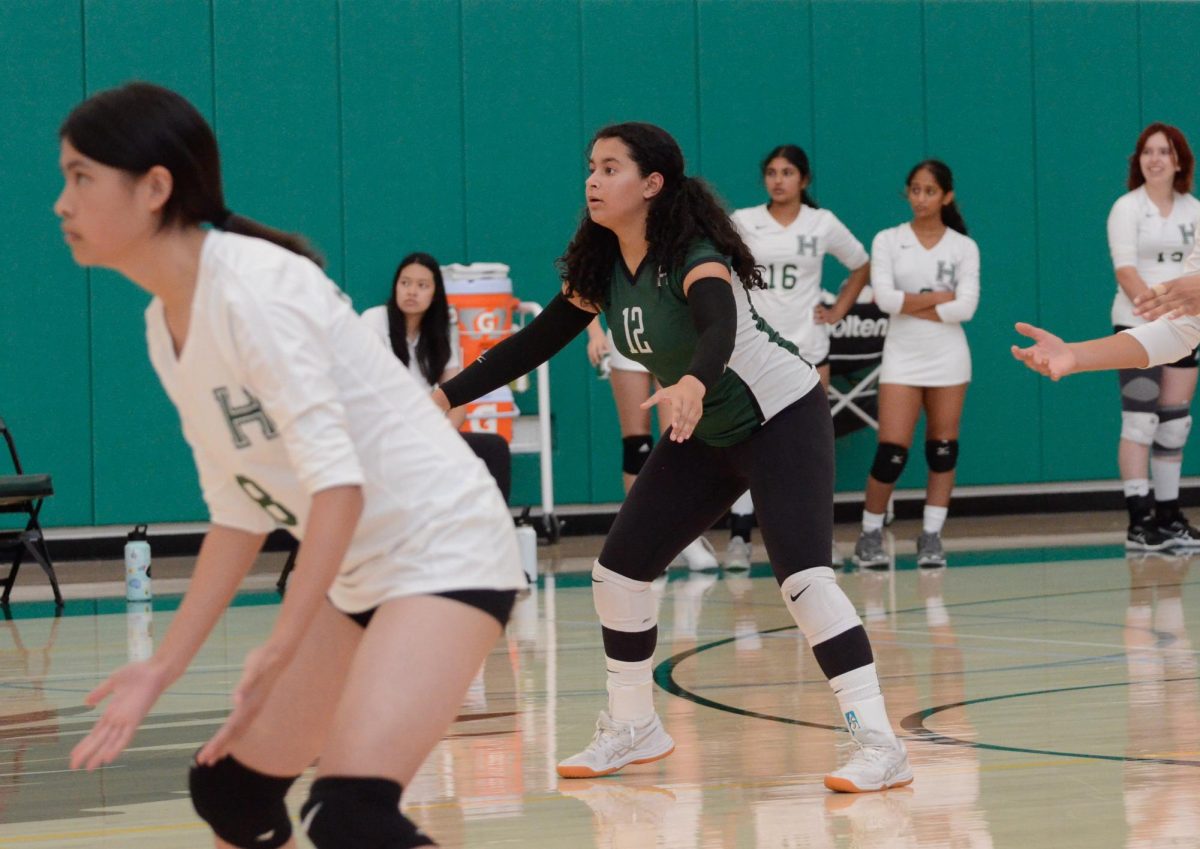 Judi Abdelrazik (10) squats down in a defensive stance, ready to receive an incoming serve. At the libero position, Judi plays in the back row and helps control possession of the ball.