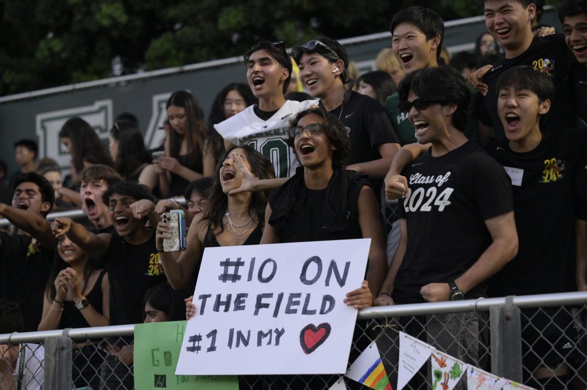 Veyd Patil (12) holds a poster for football member Ryan Barth (12). Audience members often hold posters for their friends with catchy phrases and puns.