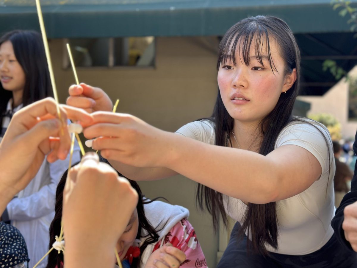 Junior Sonia Yu places a stick of spaghetti on top of her structure during a spaghetti-marshmallow tower competition today outside Manzanita Hall. The group with the tallest standing tower received gift cards.