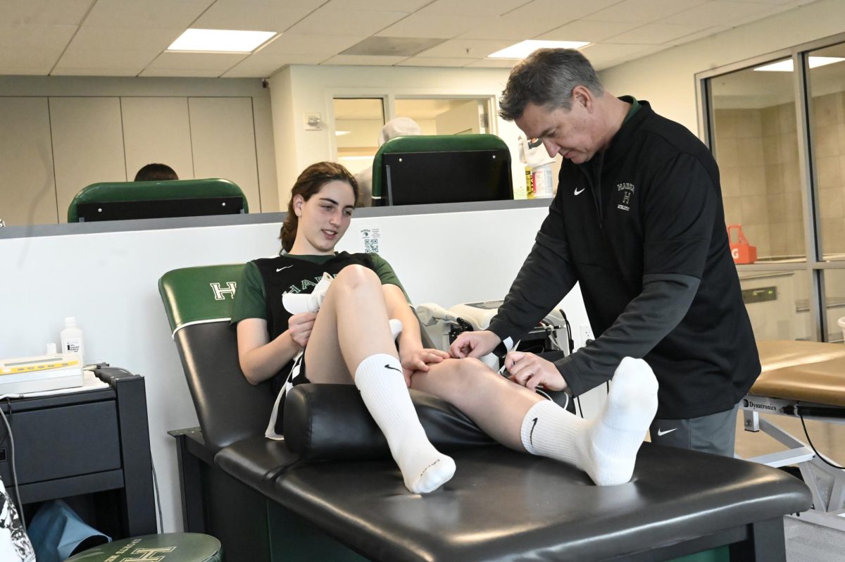 Head Athletic Trainer Wes Howard attaches the electrical muscle stimulation (EMS) machine to Emily Mitnick (11) to treat her injured hamstring. Student athletes frequent the trainers room before practices and games. 