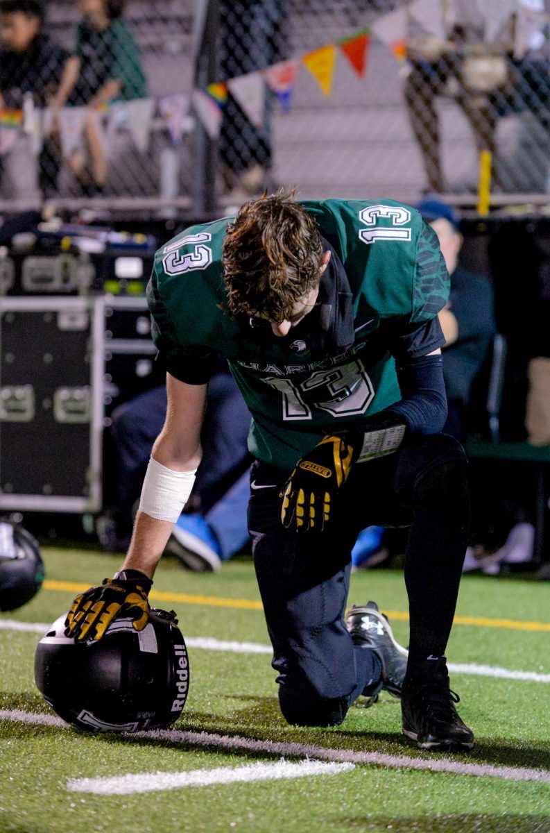 Varsity football co-captain Jack Ledford (12) kneels as an injured player receives treatment. The Eagles lost the Homecoming match against Crystal Springs Upland School 30-52. 