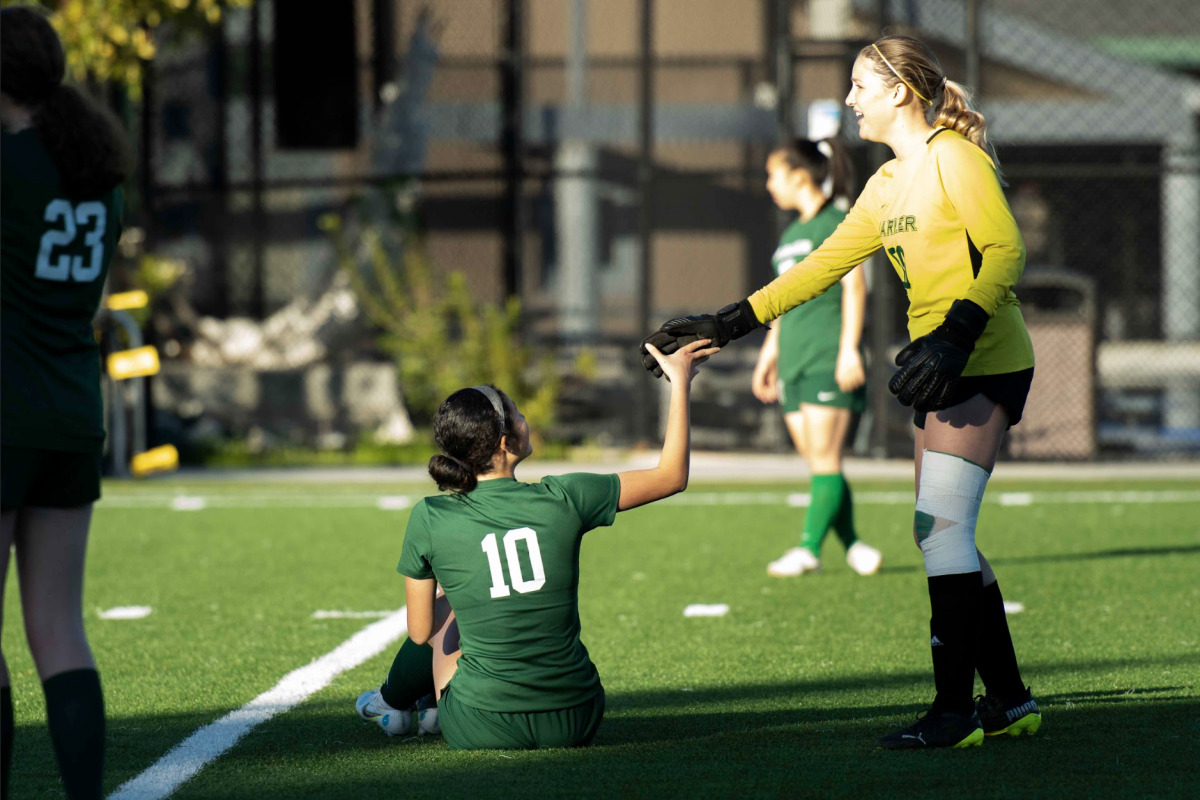 Girls varsity soccer goalie Kylie Anderson (11) gives co-captain Cynthia Wang (12) a helping hand after she paused to re-tie her shoelace. The team held fourth place in the West Bay Athletic League with a 2-3-1 league record during the 2023 season. 