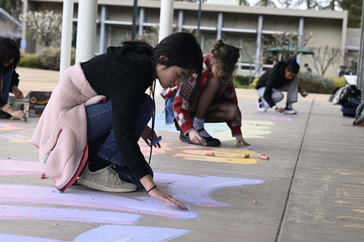 Art Club officers Emma Li (10) and Laurel Davies (12) and Student Diversity Coalition Leader Dina Ande (12) draw in chalk outside of the Rothschild Performing Arts Center on Friday. Students responded in chalk to the prompt What do you hope to see in the future?