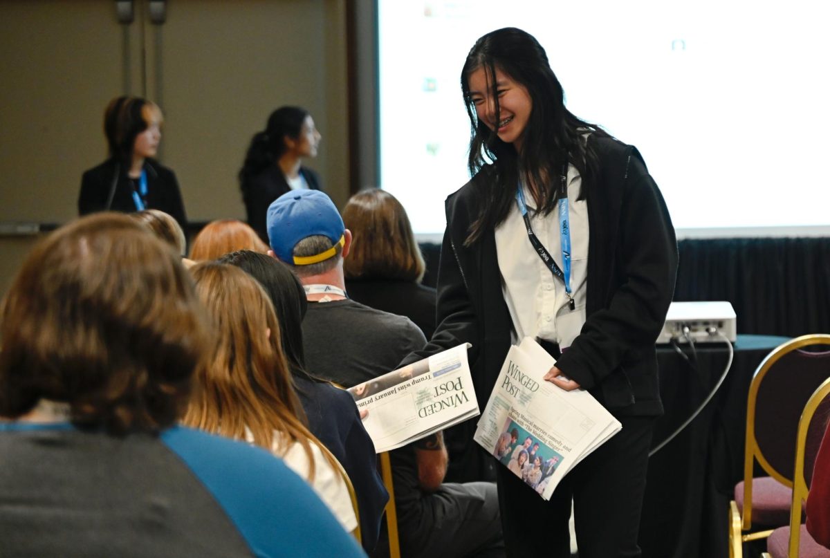 Claire Yu (10) hands out newspaper to Bring Smiles to Your Staff attendees. The presentation shared tactics to foster community and friendships.