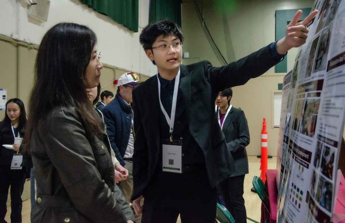 Student presenter Oliver Chen (10) talks about his project using his poster as a visual aid. Harker students from grades eight to 12 shared their research findings in the Auxiliary Gym.