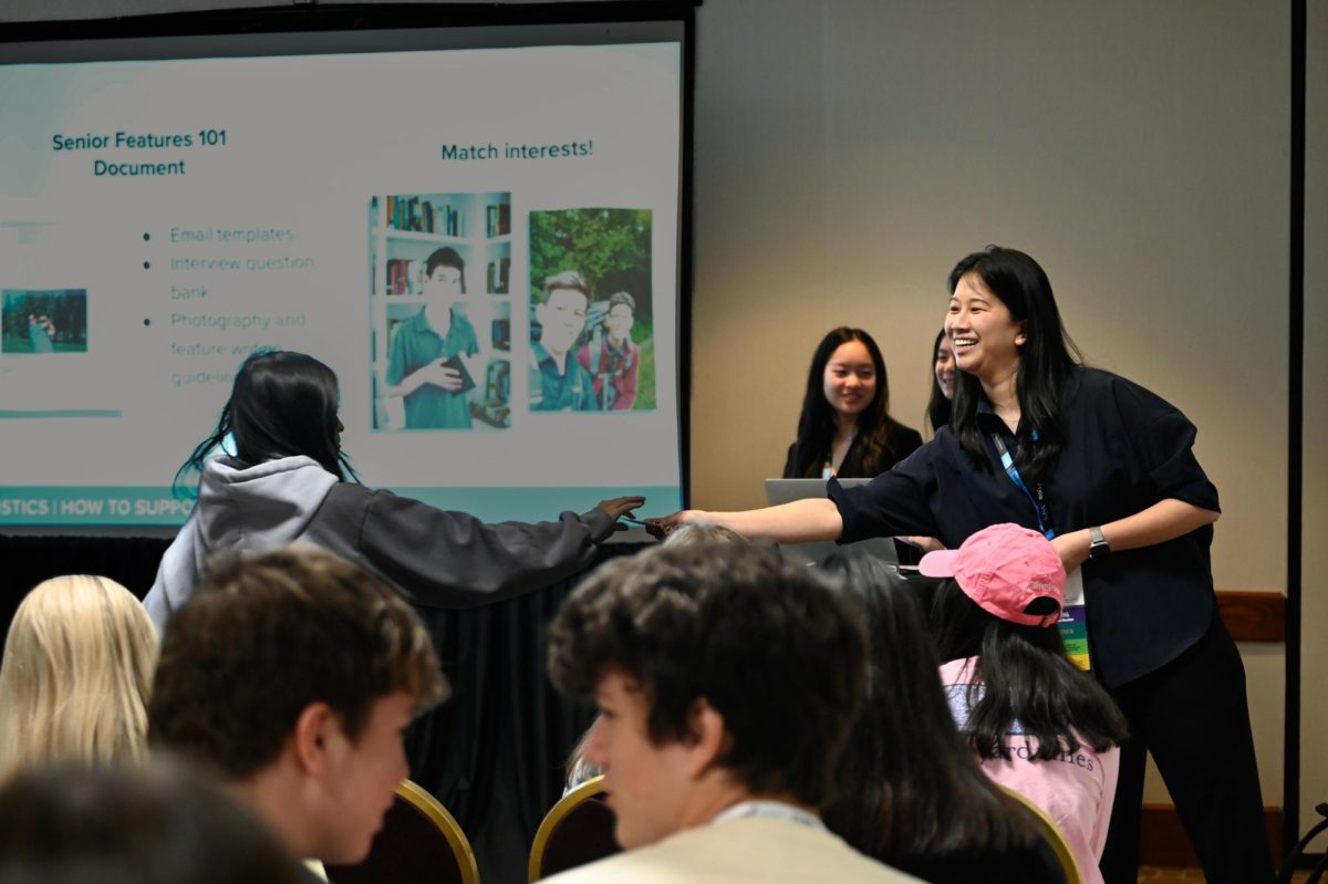 Director of Journalism Whitney Huang hands a sticker to a volunteer during the Humans of Your School session. During the presentation, the presenters held mock interviews for seniors to demonstrate the interview process of Humans of Your School.