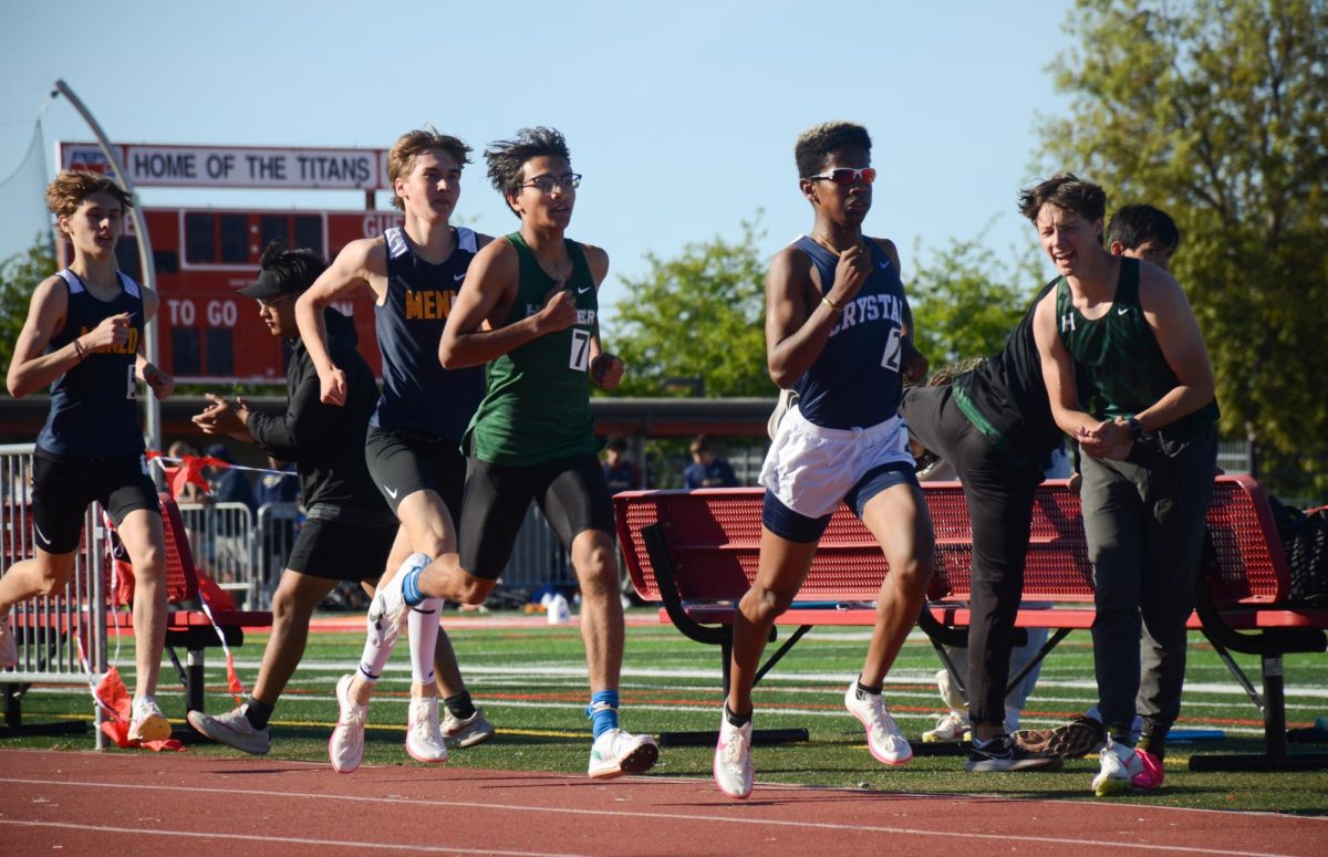 Andrew Smith (12) cheers from the sidelines as teammate Veyd Patil (12) races down the track in the varsity boys 1600-meter. Veyd placed second in his event with a time of 4:21.72.