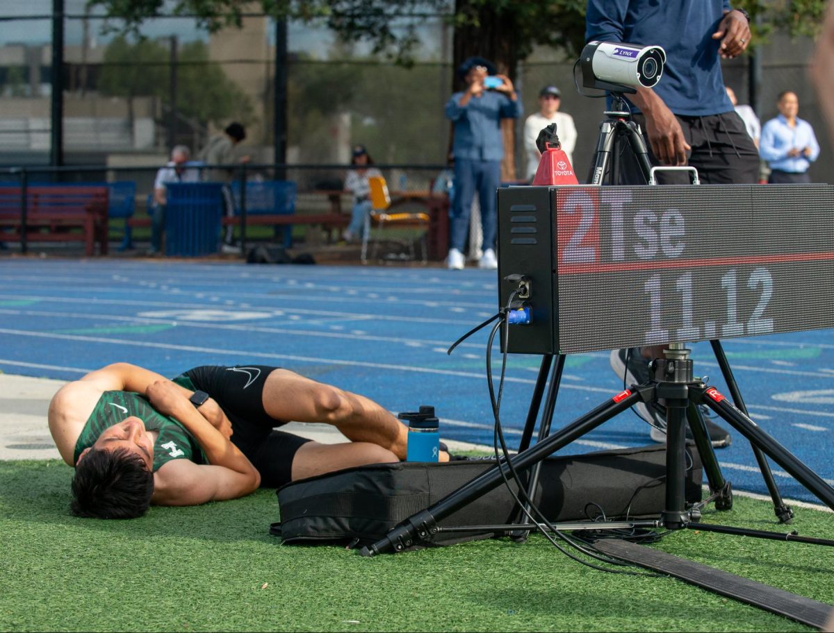 Sophomore Brady Tse lies next to the track after the 100-meter dash as the scoreboard displays his second place finish. Brady ran a new personal record, cutting down 0.2 seconds from his previous record. 