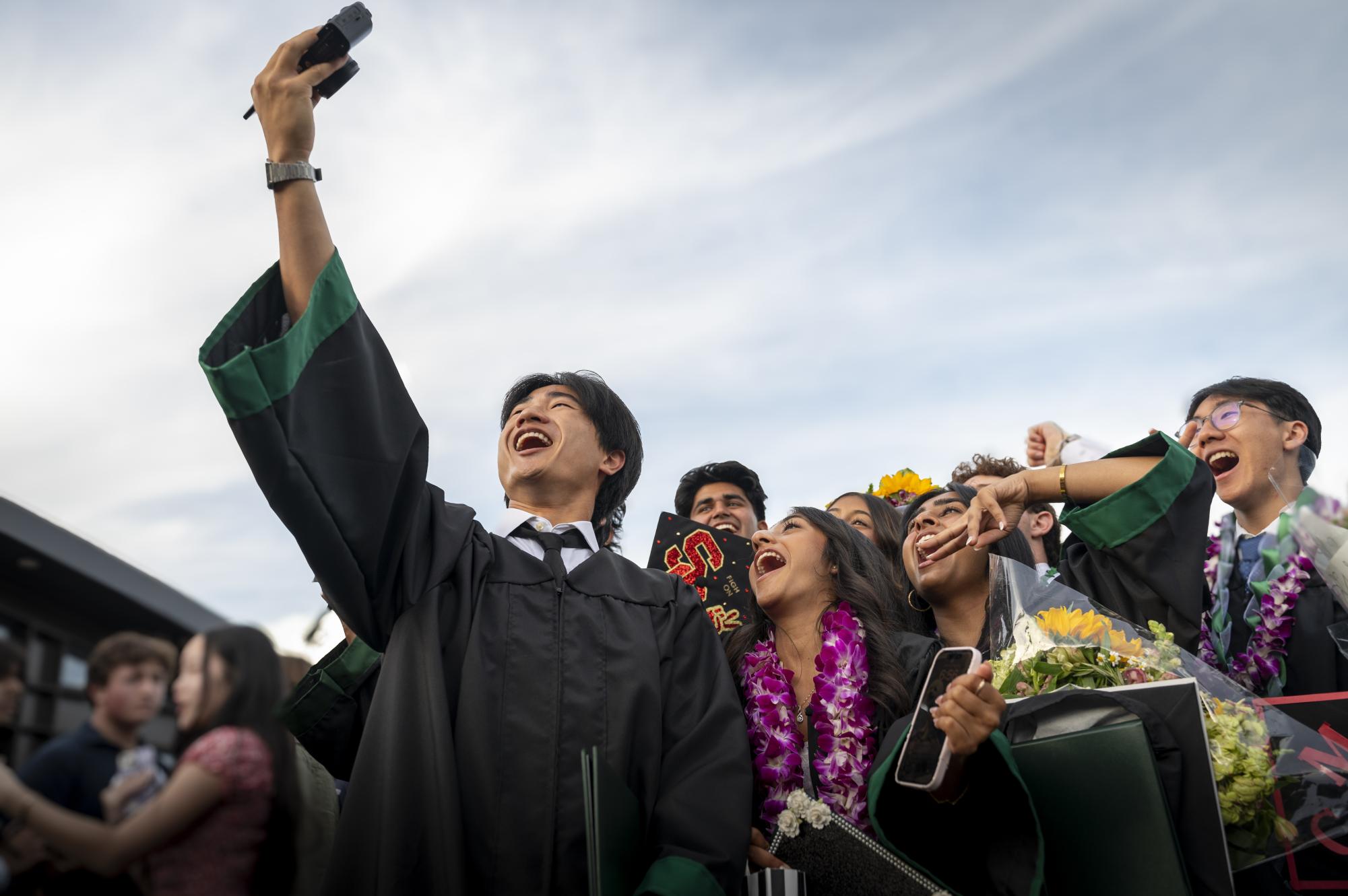 Michael Chang (24) takes a selfie on his camera as one of his final memories of senior year. Graduates mingled and took pictures in the Mountain Winerys main plaza after the ceremony.